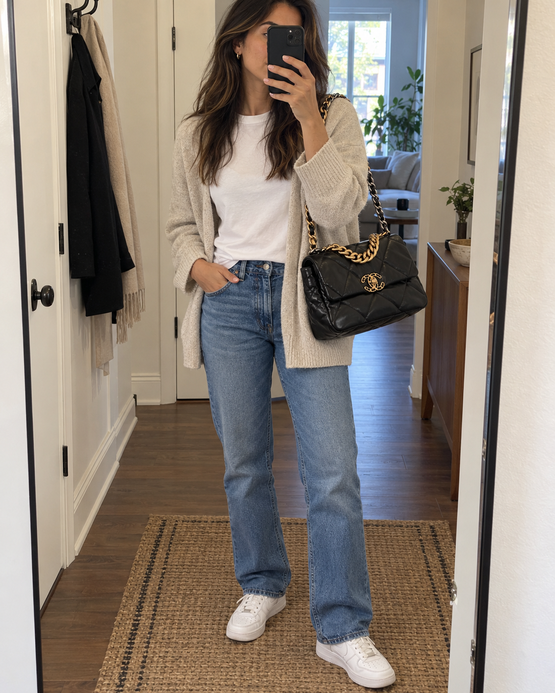 Black quilted chain bag styled with a white T-shirt, oatmeal cardigan, jeans and white sneakers.