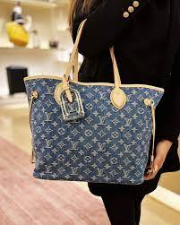 denim neverfull-style tote bag worn over shoulder with relaxed casual outfit.