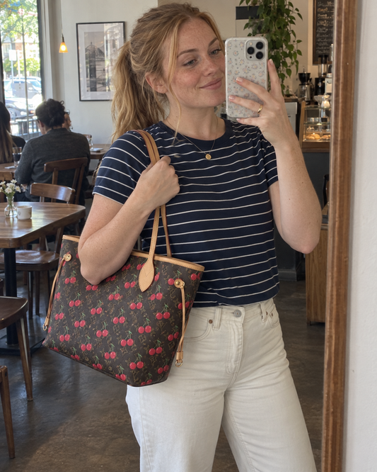 AI-generated styling illustration: cherry-print MM tote in a casual cafe outfit.